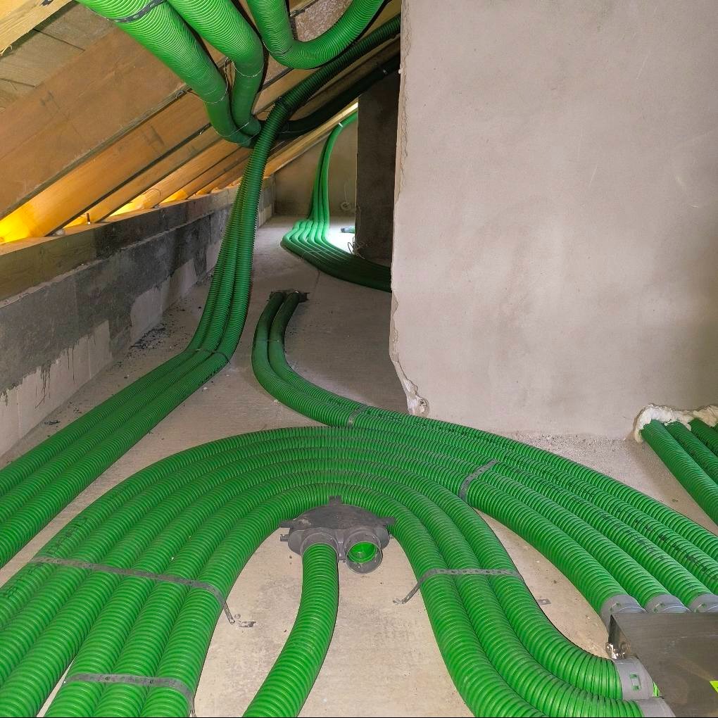 Rozprowadzenie zielonych rur wentylacyjnych w surowym wnętrzu poddasza, widoczne elementy montażowe i łączenia.