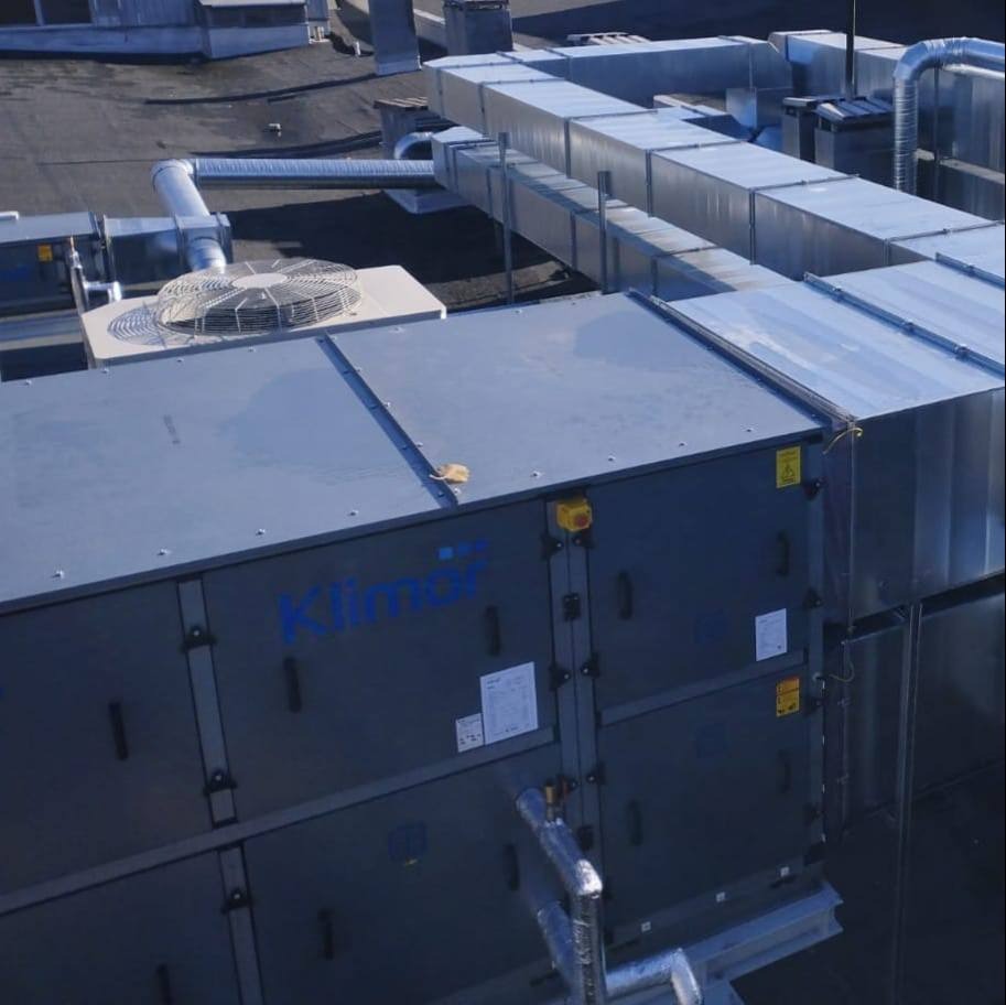 Kompleksowa instalacja wentylacyjna Klimor na dachu budynku, z widocznymi kanałami wentylacyjnymi i jednostką centralną z wentylatorem.