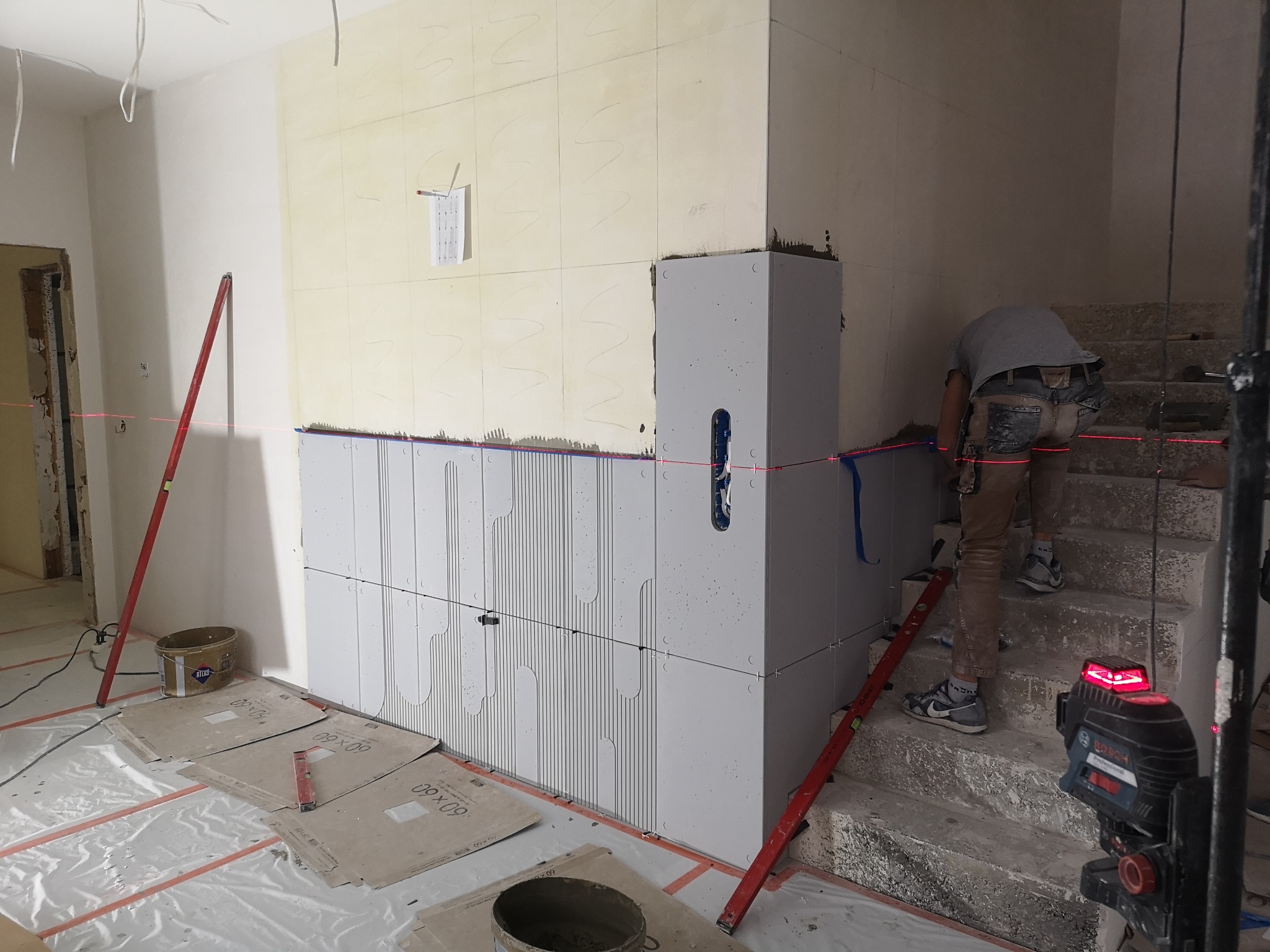 Montaż płyt imitujących beton na ścianie wewnętrznej, widoczny laser krzyżowy, poziomica i zaprawa Atlas.