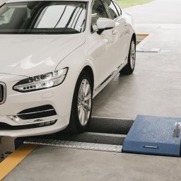 Stachurscy - Myjnia TIR Radom | Okręgowa Stacja Kontroli Pojazdów - Biały samochód Volvo na podnośniku diagnostycznym w warsztacie, widoczny fragment tablicy rejestracyjnej i logo Volvo na grillu.