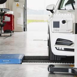 Stachurscy - Myjnia TIR Radom | Okręgowa Stacja Kontroli Pojazdów - Biały samochód na stanowisku do geometrii kół, z widocznym urządzeniem pomiarowym i płytami najazdowymi w warsztacie.