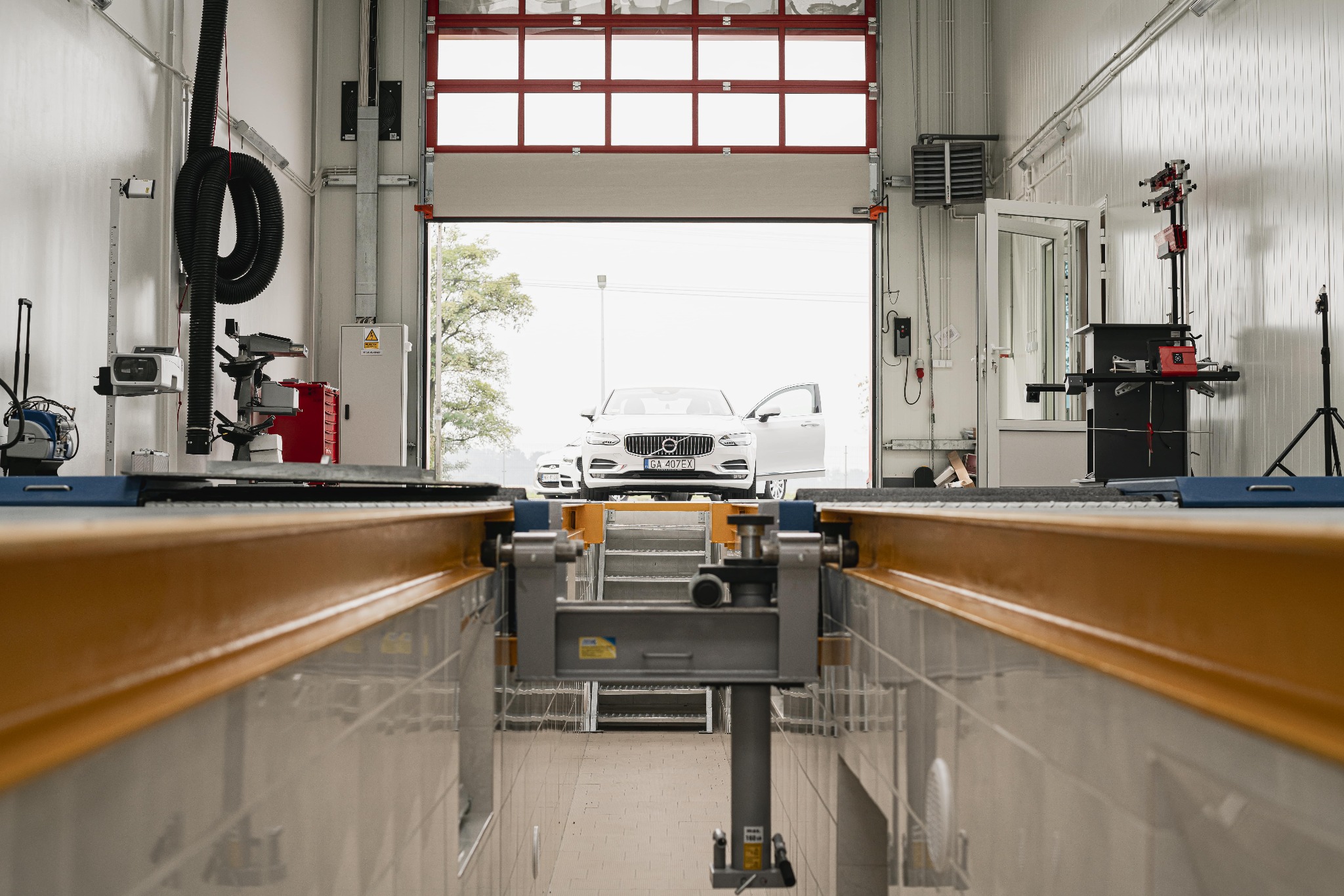 Biały samochód osobowy w warsztacie na podnośniku kanałowym, z otwartymi drzwiami po stronie kierowcy, widok z dołu kanału.