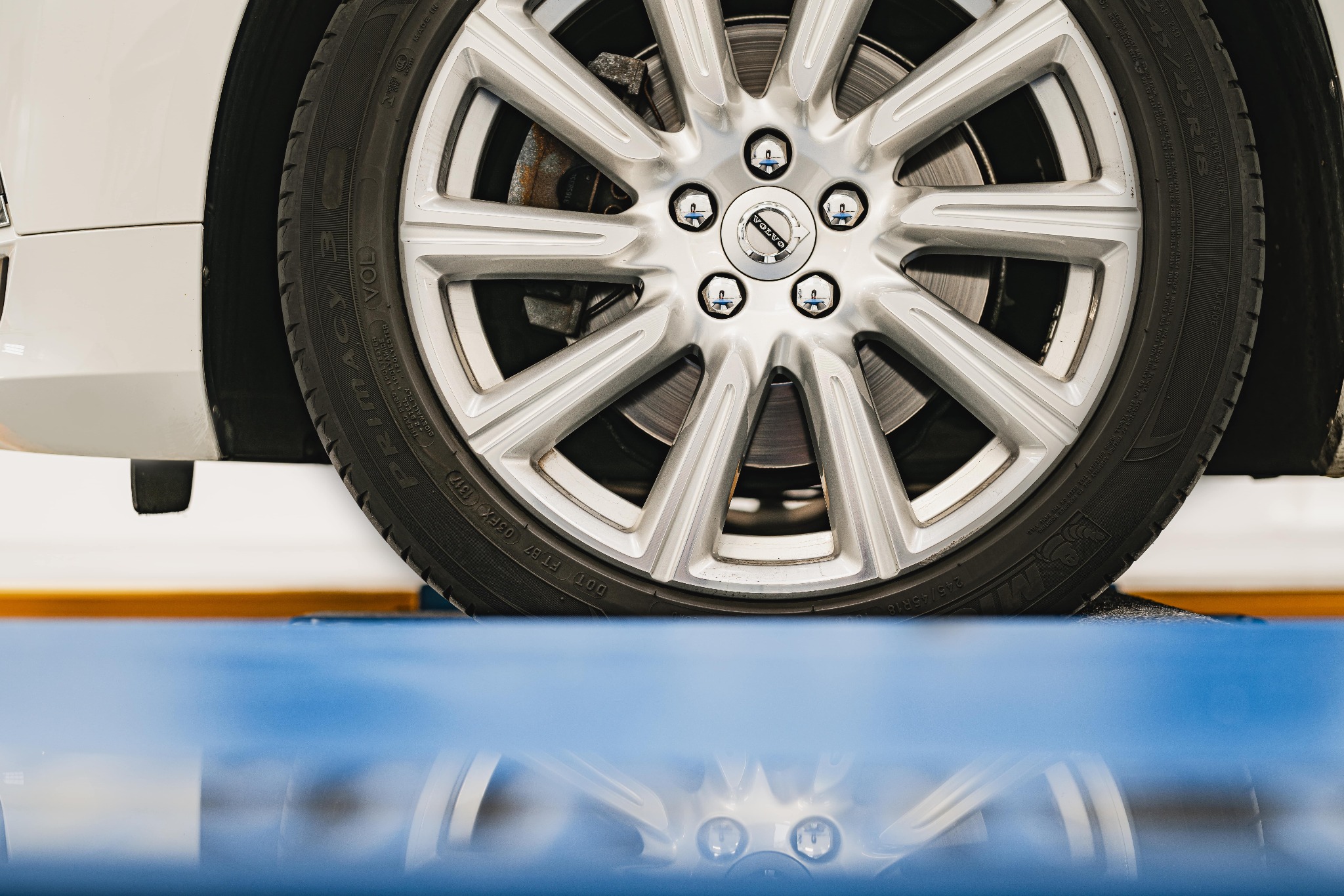 Błyszcząca felga aluminiowa z logo Volvo na białym samochodzie, stojącym na podnośniku samochodowym z niebieską platformą.