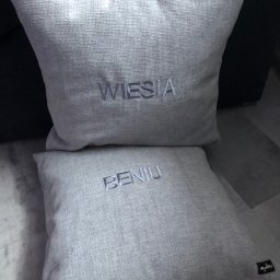 MILA SZPILA Pracownia Krawiecka Mirosława Glinka - Dwie lniane poduszki dekoracyjne z wyhaftowanymi imionami: 'Wiesia' na górnej i 'Benia' na dolnej, ustawione na podłodze.