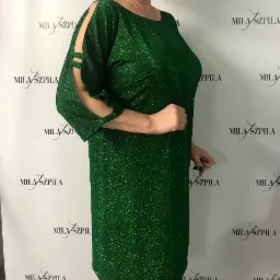 Błyszcząca, szmaragdowa sukienka mini z rozcięciami na ramionach, prezentowana na tle z powtarzającym się logo 'MILA SZPILA'.