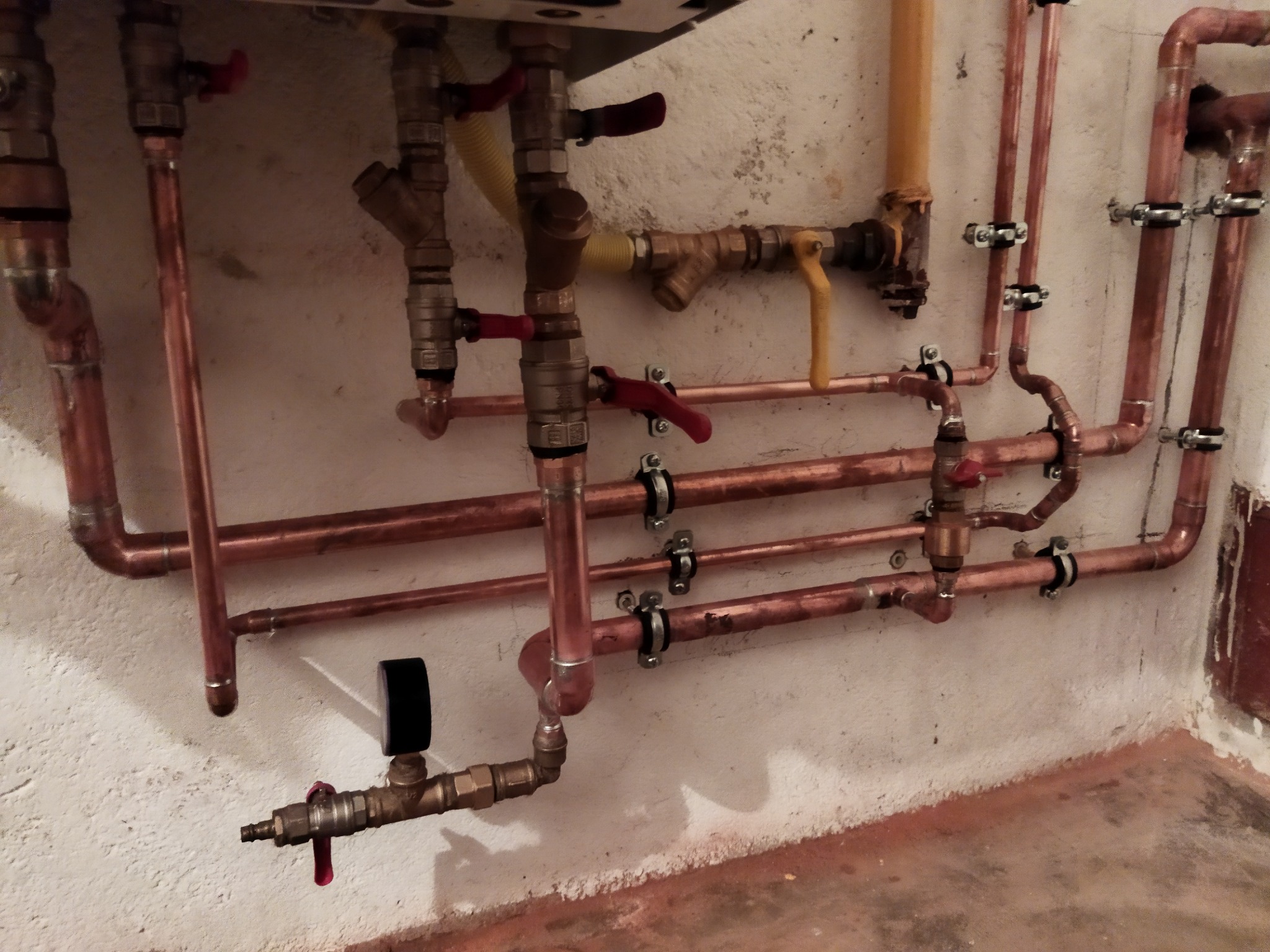 Miedziane rury centralnego ogrzewania zamontowane na ścianie z widocznymi zaworami, manometrem i elementami łączeniowymi.