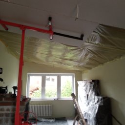 Kama-bud Usługi Ogolnobudowlane Kamil Tylkowski - Wnętrze pokoju w Przytocznej w trakcie montażu płyt kartonowo-gipsowych na suficie, zabezpieczone folią, widoczny podnośnik do płyt oraz drabina.