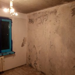 Kama-bud Usługi Ogolnobudowlane Kamil Tylkowski - Pokój przed remontem: stare, zniszczone ściany z odpadającym tynkiem, okno zabezpieczone folią malarską, goła podłoga, widoczny grzejnik i oświetlenie sufitowe