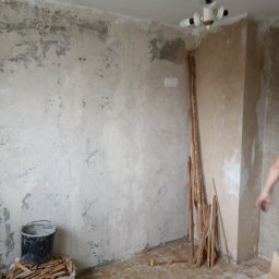 Kama-bud Usługi Ogolnobudowlane Kamil Tylkowski - Pokój w trakcie przygotowania do prac wykończeniowych; surowe ściany z pozostałościami starej farby, widoczne wiadra z resztkami materiałów, listwy przypodłogowe oparte o ścianę, podłoga...