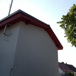 Ocieplony budynek z czerwoną podbitką, widoczny fragment elewacji, rynna i drzewo w tle.