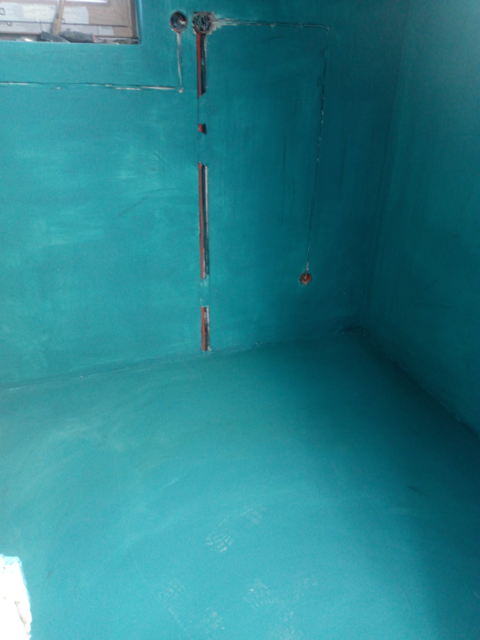 Świeżo pomalowana łazienka na turkusowo, widoczne ślady po stopach na podłodze i przygotowane kable elektryczne w ścianie.