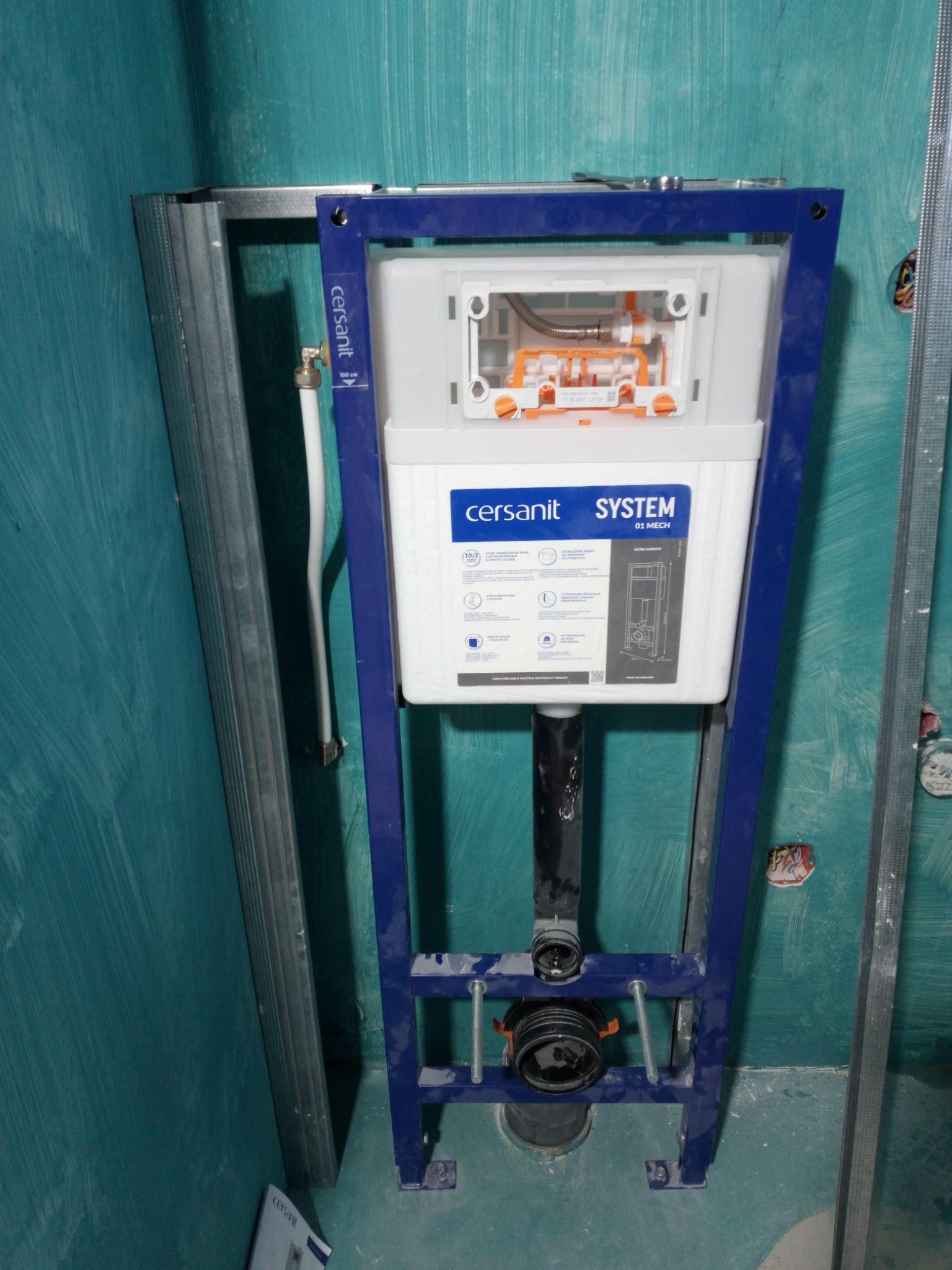 Stelaż podtynkowy Cersanit System 01 Mech zamontowany na tle turkusowej ściany w trakcie prac wykończeniowych łazienki, widoczna instalacja wodno-kanalizacyjna oraz profile do montażu płyt...