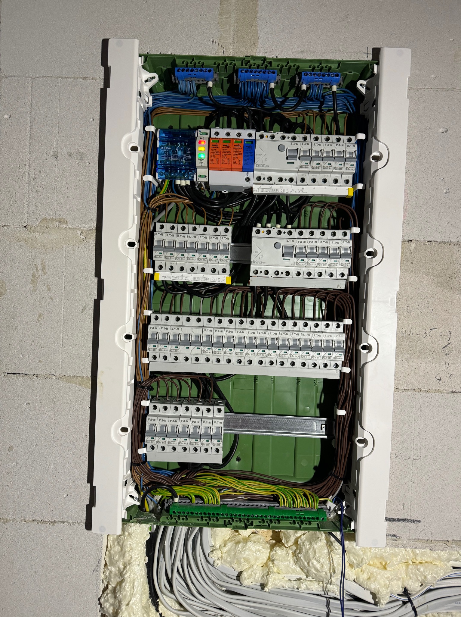 Rozdzielnica elektryczna z zainstalowanymi zabezpieczeniami, przewodami i modułami, zamontowana na ścianie z betonu komórkowego wewnątrz budynku.