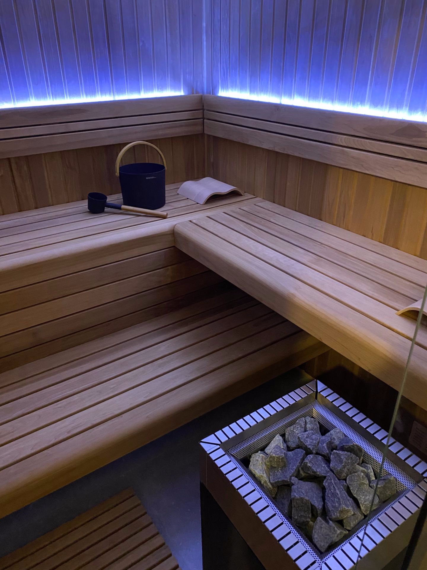 Wnętrze wykończonej drewnem, oświetlonej niebieskim światłem, z piecem na kamienie, wiadrem i chochlą