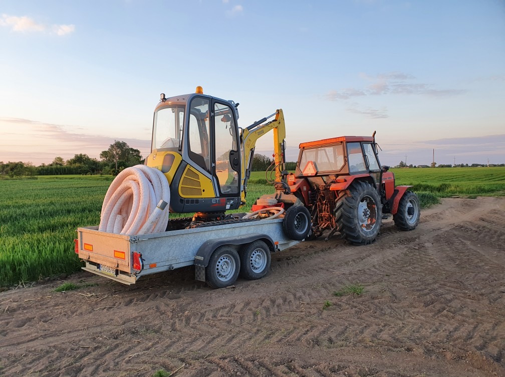 Mini koparka i traktor na przyczepie w Głownie, z rolką rur karbowanych, gotowe do transportu na miejsce robót.