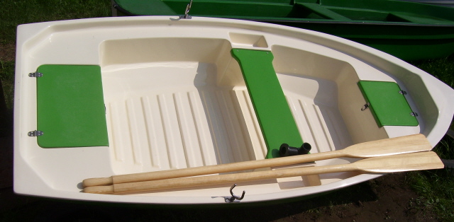 Biała łódź wiosłowa z zielonymi elementami wyposażenia i parą drewnianych wioseł leżących wewnątrz, widok z góry.