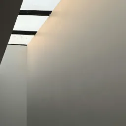 Wnętrze z gładkimi, pomalowanymi na jasny odcień ścianami, oświetlone przez okno dachowe z czarnymi ramami, ukazujące minimalistyczny kąt pomieszczenia.