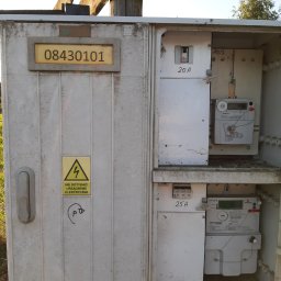 Instalatorstwo Elektryczne Pomiary Elektryczne Wojciech Zienkiewicz - Otwarta skrzynka elektryczna z dwoma licznikami energii, bezpiecznikami 20A i 25A, tabliczką z numerem 08430101, naklejką ostrzegawczą 'Nie dotykać urządzenia elektryczne' i amatorskim rysunkiem...