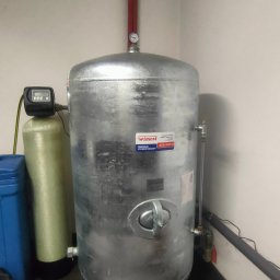 HydroX - Srebrny zbiornik hydroforowy marki Wimest w kotłowni, obok zielony filtr wody, widoczne narzędzia na podłodze.