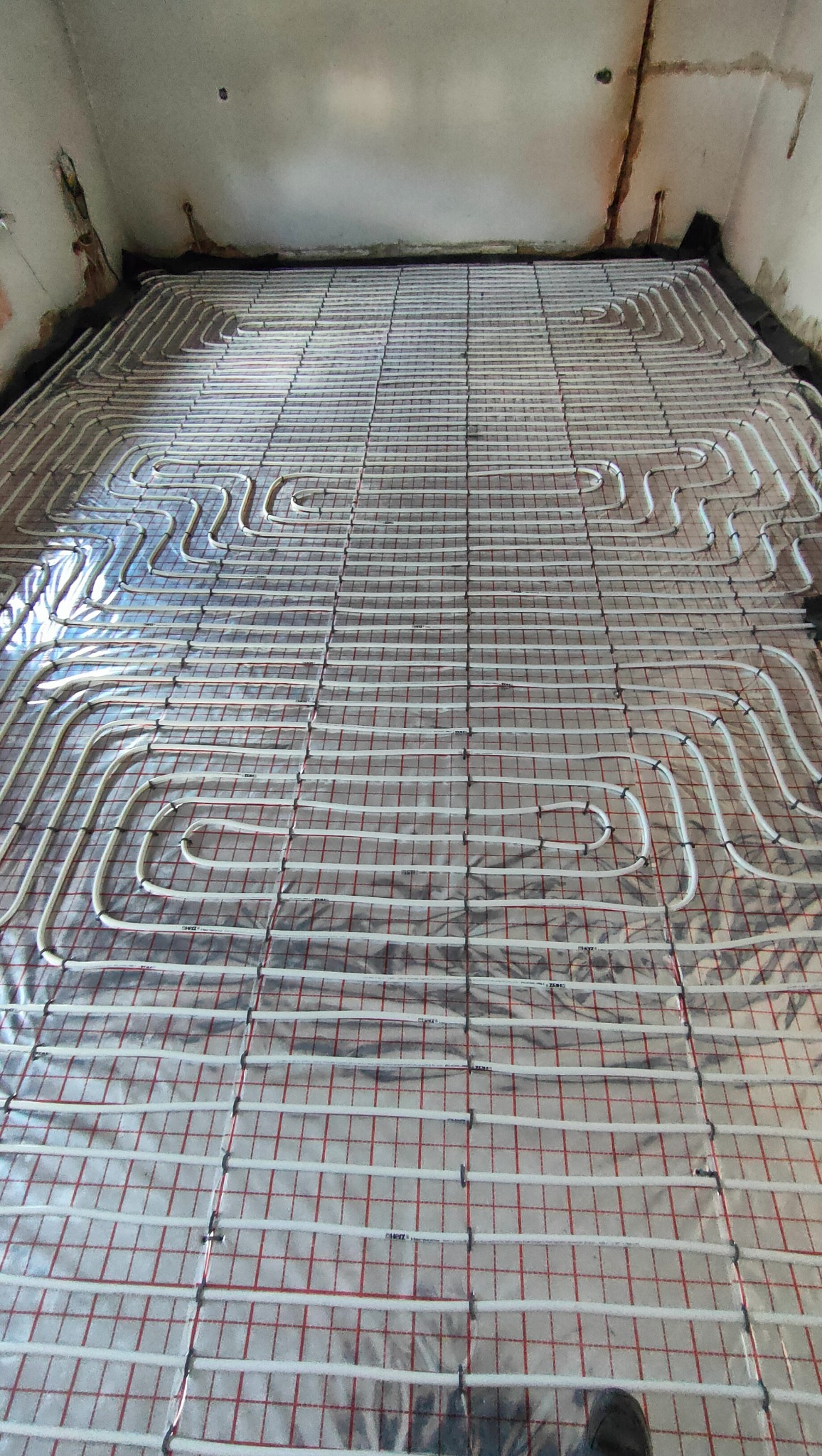 Instalacja ogrzewania podłogowego w trakcie realizacji w Babienicy: rury grzewcze ułożone na folii z siatką, widoczne przygotowania do wylewki.