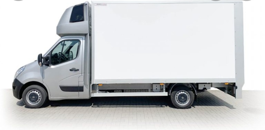 Srebrny samochód dostawczy z białą zabudową kontenerową, zaparkowany na kostce brukowej, widok z boku.