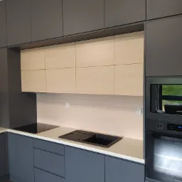 Nowoczesna kuchnia w odcieniach szarości z jasnymi, drewnopodobnymi górnymi szafkami, czarnym zlewem i płytą indukcyjną, oraz wbudowanym piekarnikiem Samsung.