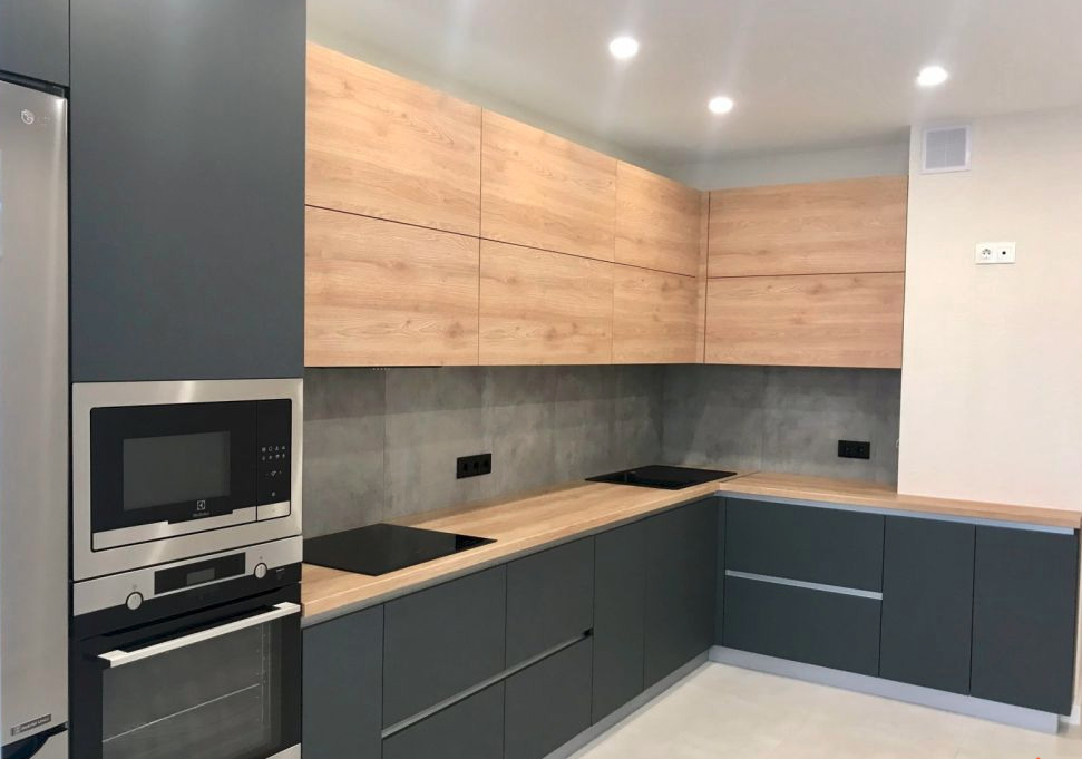 Nowoczesna kuchnia z szarymi dolnymi szafkami i drewnopodobnymi górnymi, płyta indukcyjna w blacie, zabudowa piekarnika i mikrofalówki.