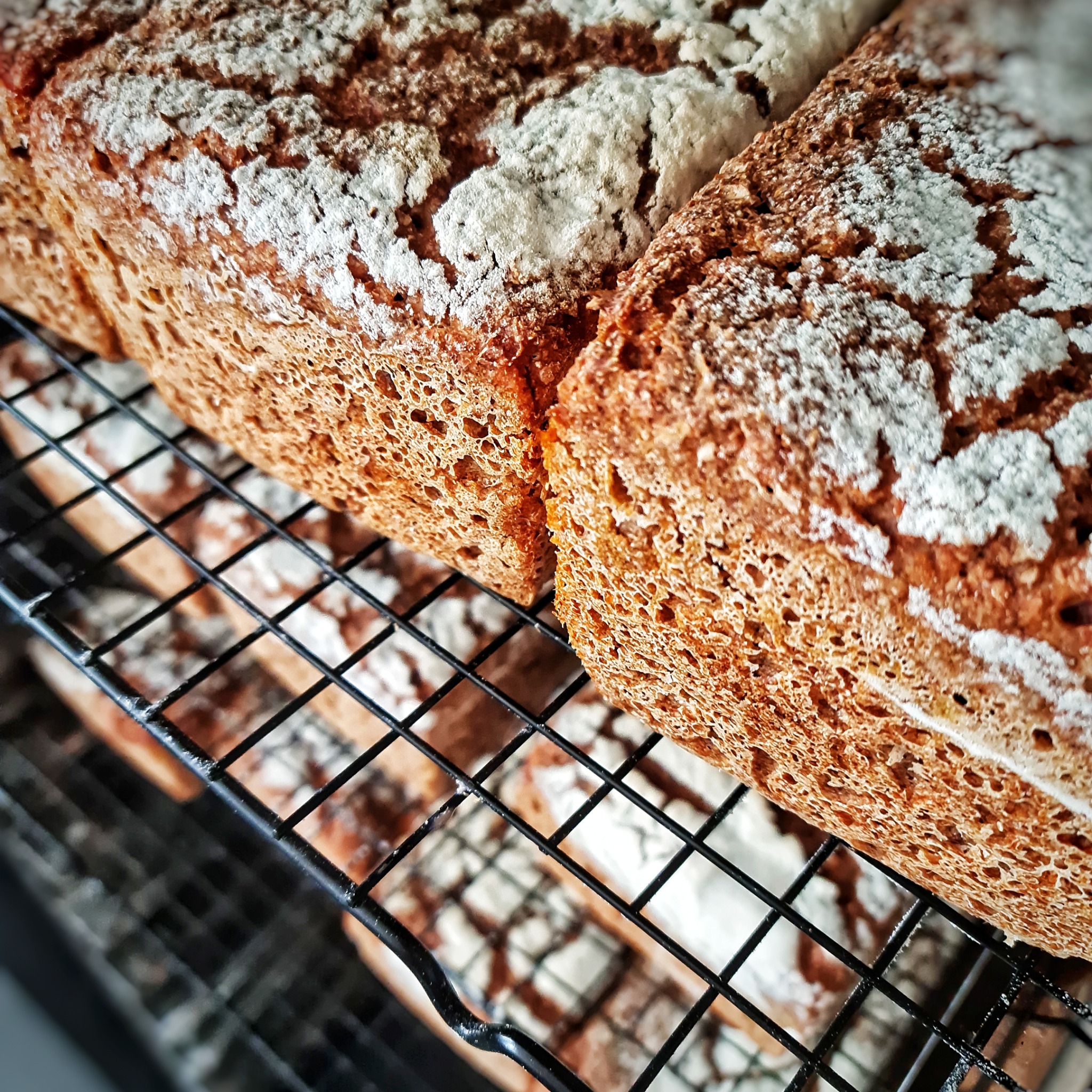 Świeżo upieczony, razowy chleb posypany mąką, ułożony na metalowej kratce do studzenia.