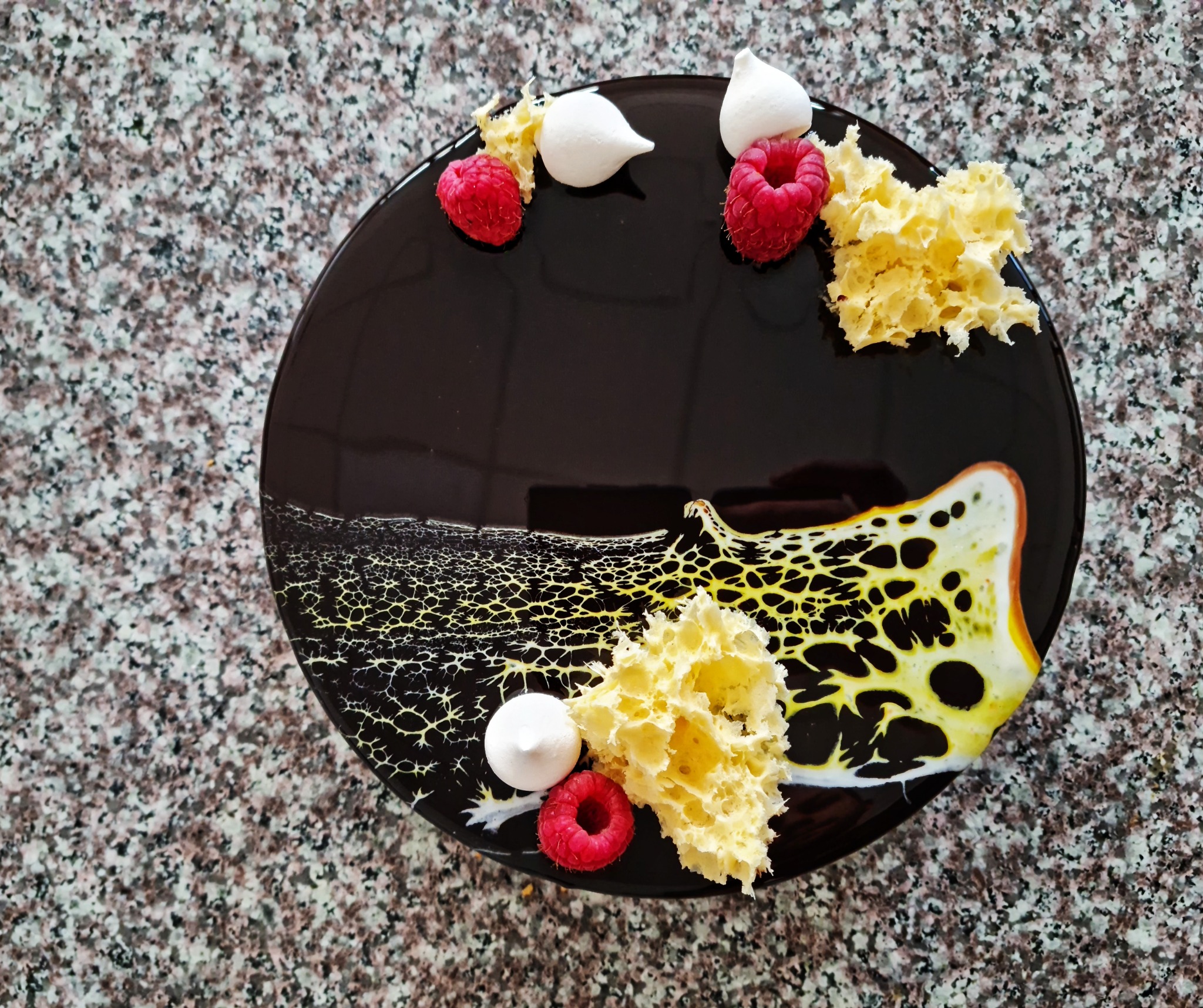 Elegancki deser z malinami, bezami i dekoracyjną glazurą na czarnym talerzu, prezentowany przez cukiernię z Łodzi.