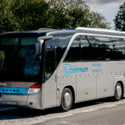 Szary autobus marki Setra z oznaczeniami szkoły nauki jazdy Centrum, zaparkowany na poboczu drogi z kostki brukowej, w tle zieleń drzew.