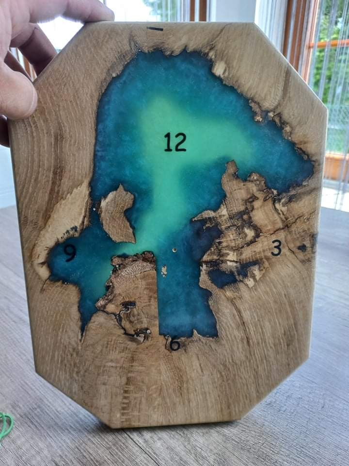 Drewniany zegar z żywicą epoksydową w odcieniach turkusu, cyfry 12, 3, 6, 9, widoczne słoje drewna i nieregularny kształt.