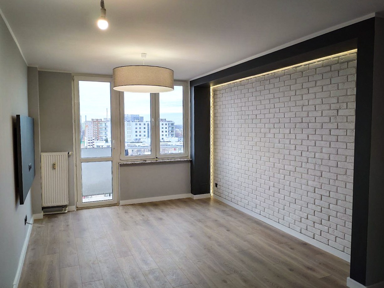 Jasne wnętrze pokoju z panelami podłogowymi, białą cegłą na ścianie z podświetleniem LED, szarą ścianą i dużym oknem z widokiem na miasto.