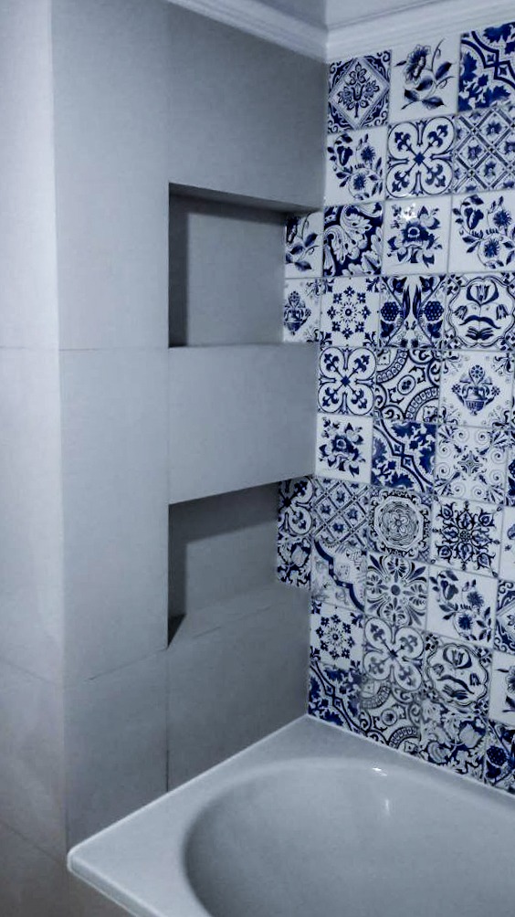 Narożnik łazienki z zabudowaną wnęką i ścianą wyłożoną dekoracyjnymi, biało-niebieskimi płytkami ceramicznymi z motywami roślinnymi i geometrycznymi, widoczny fragment wanny.