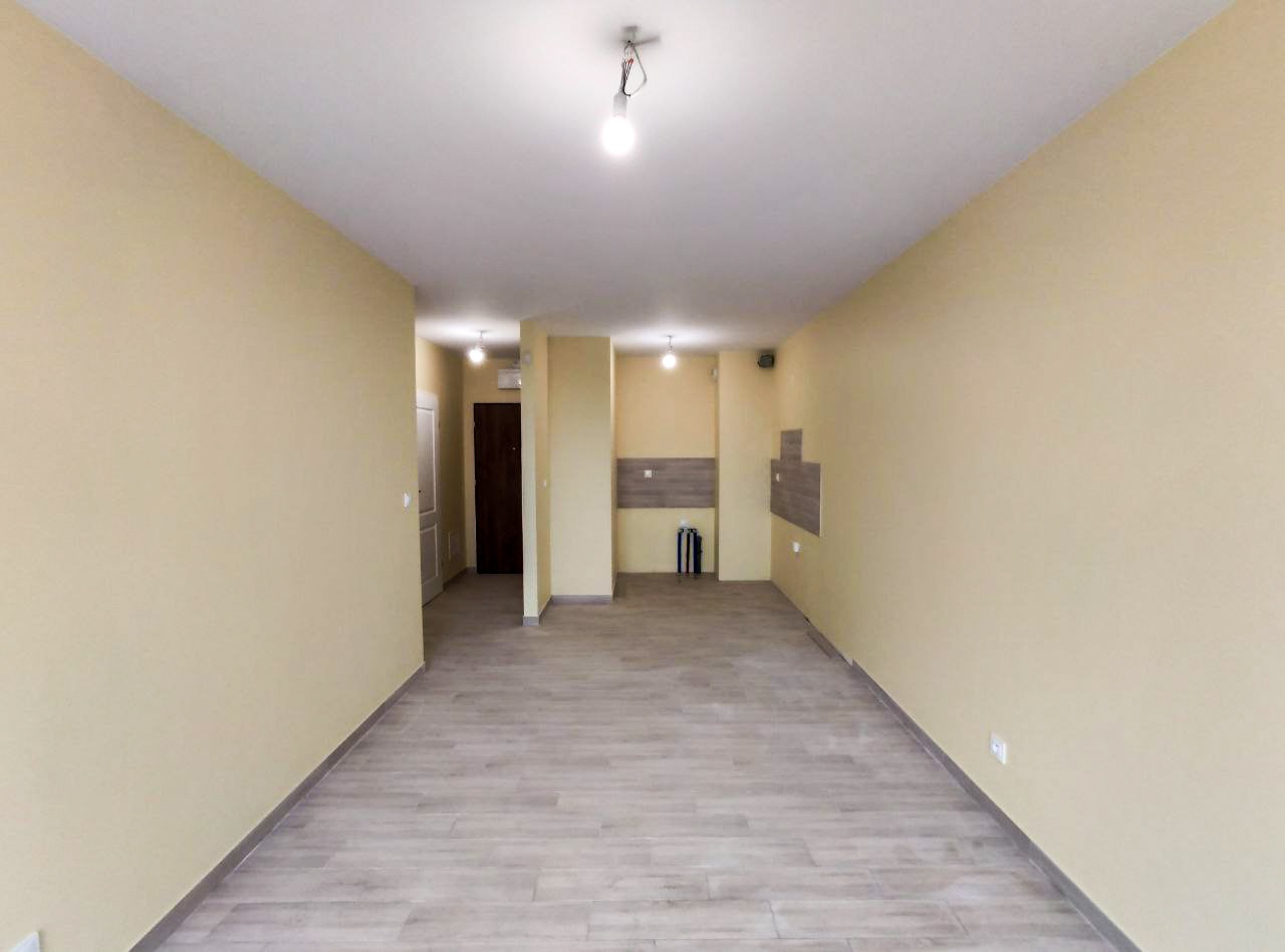 Pomalowane na jasnożółto puste pomieszczenie z panelami podłogowymi w odcieniach szarości, z widocznymi fragmentami przygotowanej pod zabudowę ściany w tle.