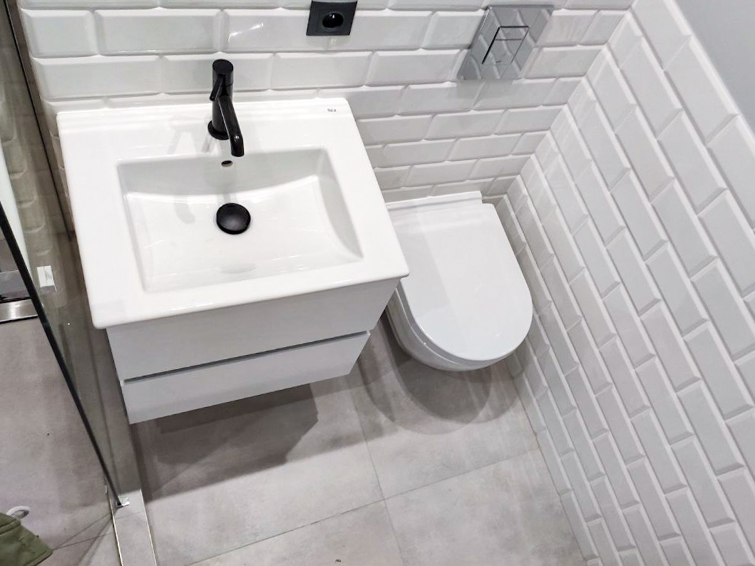 Nowoczesna łazienka z białą umywalką z czarną baterią, podwieszaną toaletą i białymi płytkami typu metro na ścianach.