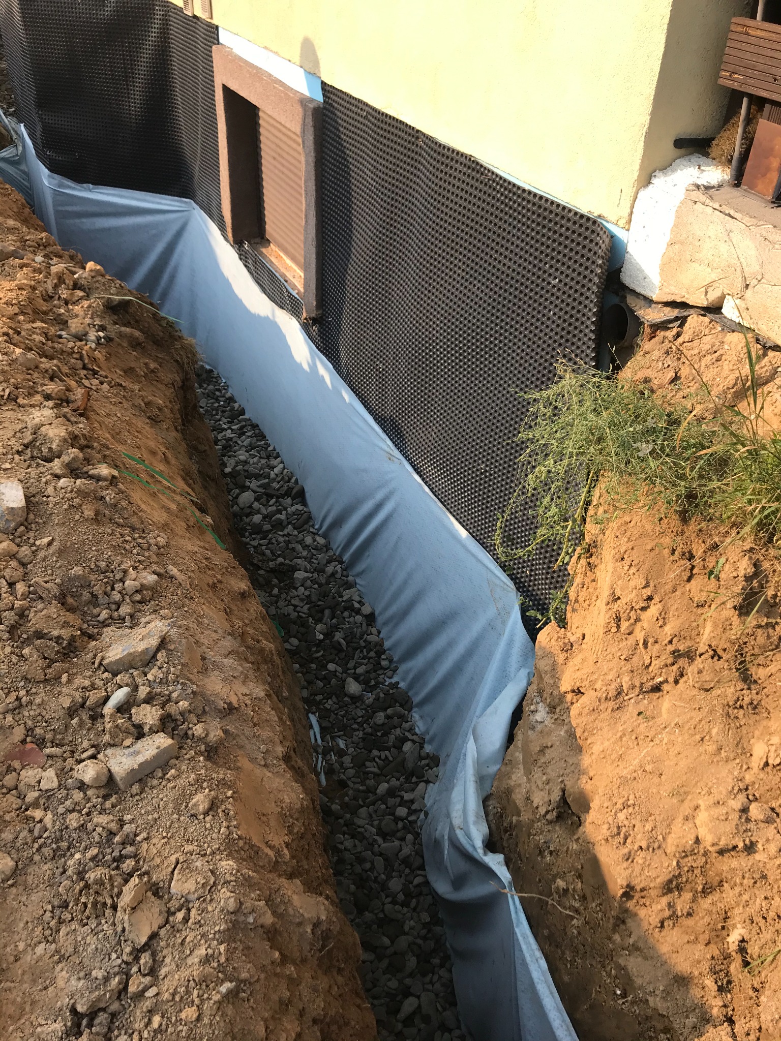 Fundament budynku zabezpieczony folią kubełkową i obsypany żwirem, widoczny wykop w ziemi.