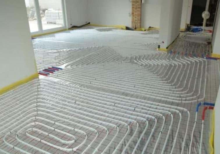 Rozłożone rury ogrzewania podłogowego na siatce w surowym wnętrzu, przygotowane do zalania wylewką.