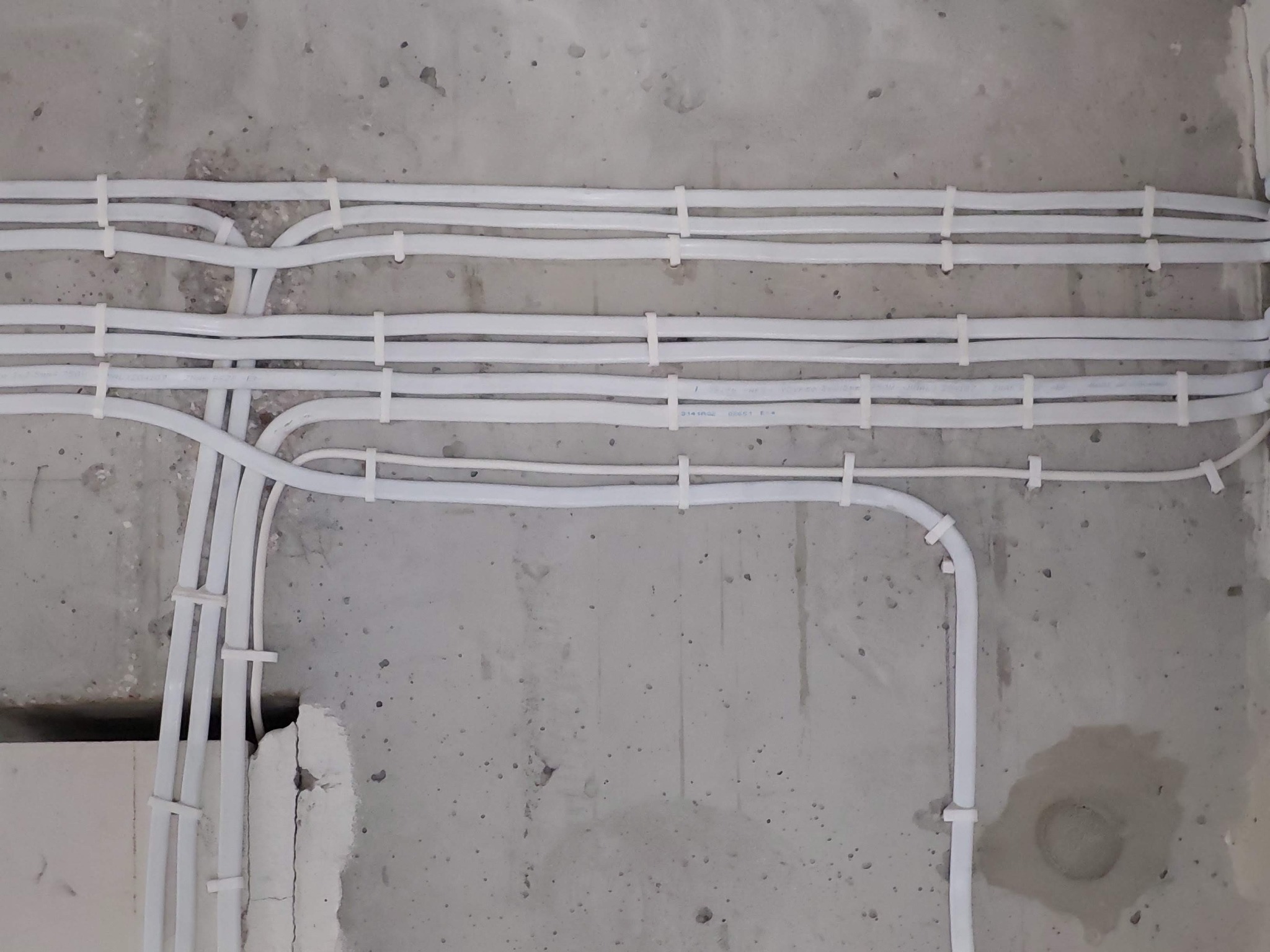 Białe przewody elektryczne przymocowane do surowego, betonowego sufitu za pomocą białych uchwytów, widoczne z bliska.