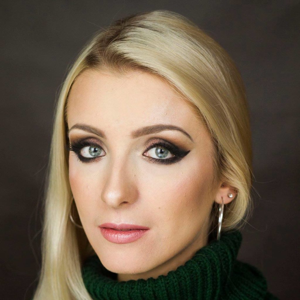 Portret blondynki z intensywnym, wieczorowym smoky eye w odcieniach brązu i czerni, podkreślonym czarnym eyelinerem, noszącej zielony sweter z golfem.
