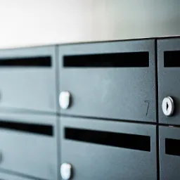 Rząd nowoczesnych, metalowych skrzynek pocztowych wewnątrz budynku, z numerem '7' na jednej ze skrzynek, oświetlonych delikatnym światłem.