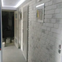 Korytarz po remoncie: biała cegła na ścianie, szare płytki na podłodze, dwoje drzwi wewnętrznych i oświetlenie sufitowe LED. Widoczne puszki elektryczne.