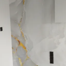 Ściana wykończona płytą imitującą biały marmur z wyraźnymi złotymi żyłami, widoczne gniazdko elektryczne i fragment podłogi z szarymi panelami.