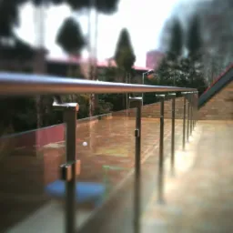 Szklana balustrada z metalowymi słupkami na tarasie z widokiem na zieleń, z widoczną białą piłeczką na podłodze.