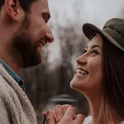 Uśmiechnięta para trzymająca się za ręce, zbliżenie na twarze, kobieta w czapce.