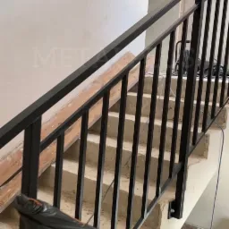 Czarne, metalowe balustrady schodowe zamontowane w surowym wnętrzu klatki schodowej w trakcie remontu, widoczne przewody i zabezpieczenia.