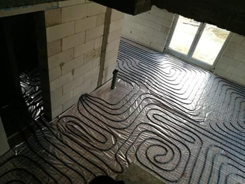 Rury czarnego ogrzewania podłogowego ułożone na srebrnej folii izolacyjnej w surowym wnętrzu budynku z oknem.