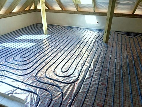 Montaż rur na folii z siatką pod system grzewczy w pomieszczeniu z drewnianą konstrukcją dachu.