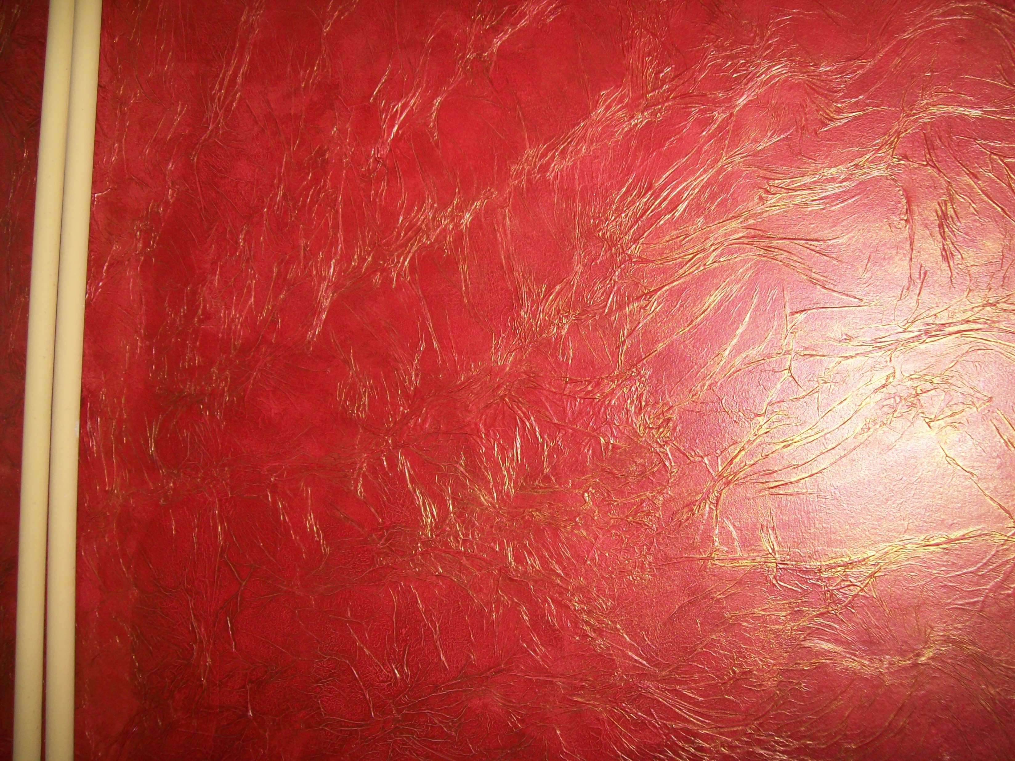 Czerwona ściana z dekoracyjną fakturą i złotymi żyłkami, obok pionowo ułożone dwie białe listwy przypodłogowe.