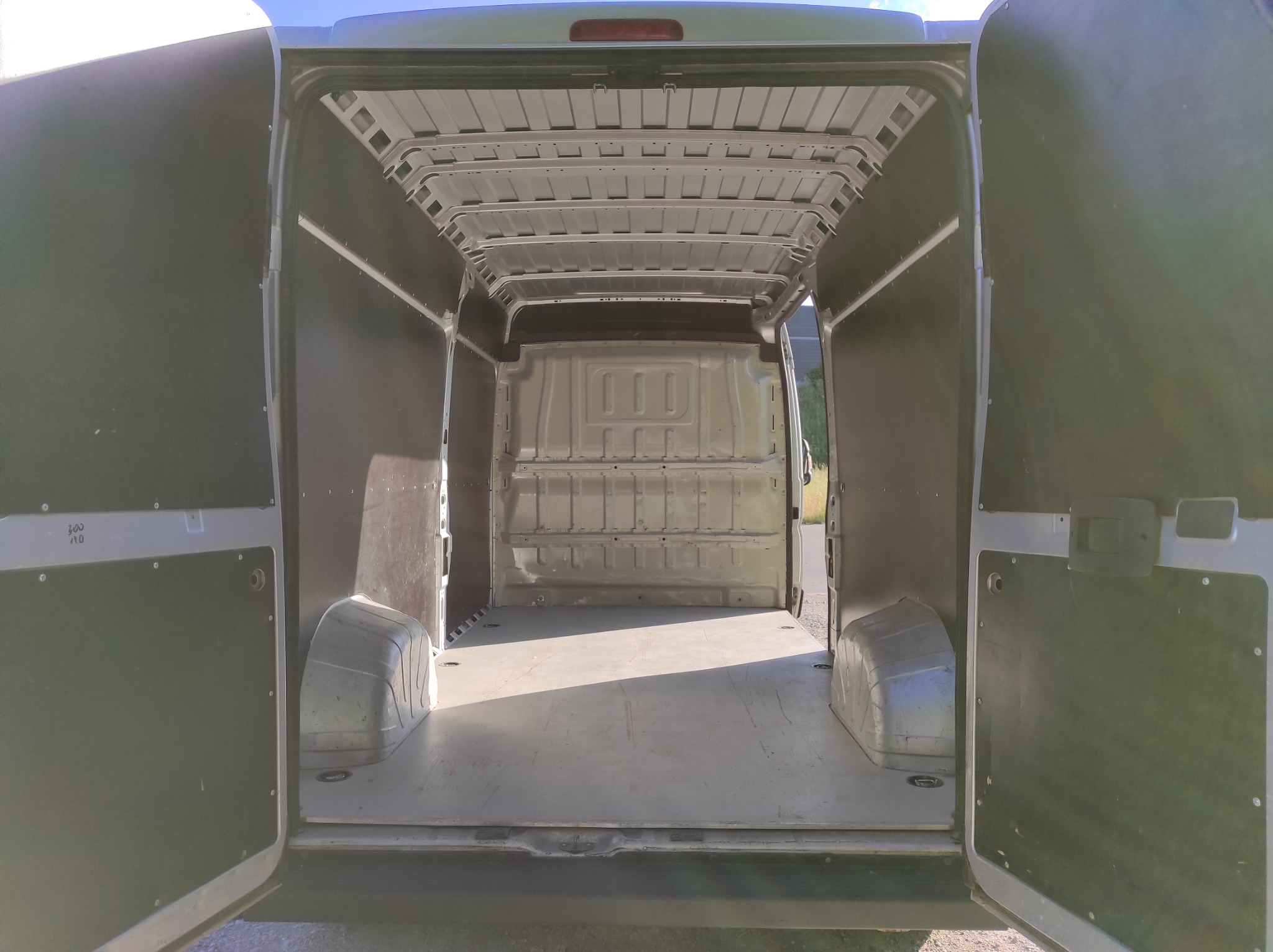 Wnętrze pustej furgonetki z otwartymi tylnymi drzwiami, widok z zewnątrz, oświetlenie dzienne.