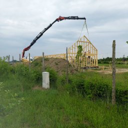 Twój Dom Szkieletowy - Montaż szkieletu domu z drewna przy użyciu dźwigu na tle zieleni i pochmurnego nieba.